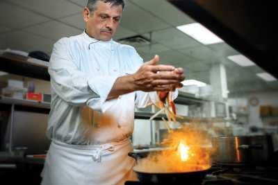 man putting some food into frying pan that is on fire